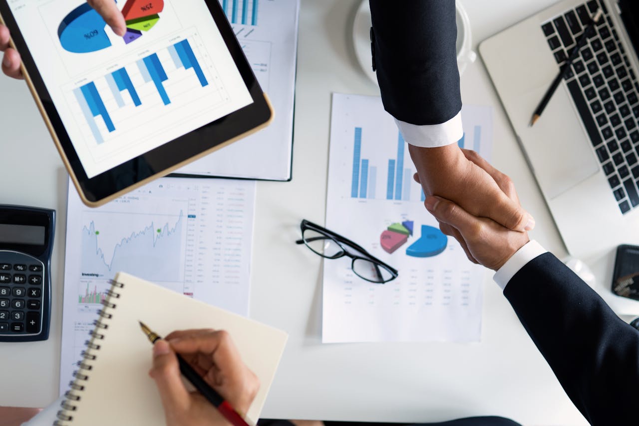 gallery-01 Business professionals handshake over graphs and charts in a corporate setting, symbolizing successful negotiation and agreement.